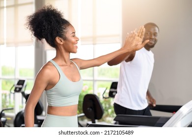 Black African American couple clapping hands together while running on the treadmill at fitness club. Healthy lifestyle, training in gym. Fitness partners give a high five. healthy concept