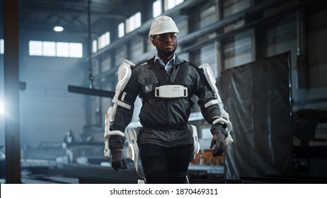 Black African American Engineer Is Testing A Futuristic Bionic Exoskeleton And Proudly Wearing It In A Heavy Steel Industry Factory. Successful Contractor Walking In A Powered Mobile Machine Shell.