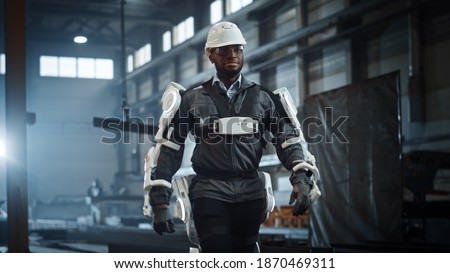 Black African American Engineer is Testing a Futuristic Bionic Exoskeleton and Proudly Wearing it in a Heavy Steel Industry Factory. Successful Contractor Walking in a Powered Mobile Machine Shell.