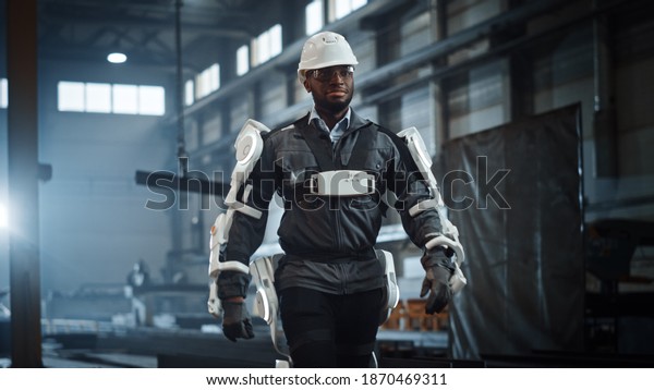 Black African American Engineer is Testing a\
Futuristic Bionic Exoskeleton and Proudly Wearing it in a Heavy\
Steel Industry Factory. Successful Contractor Walking in a Powered\
Mobile Machine Shell.