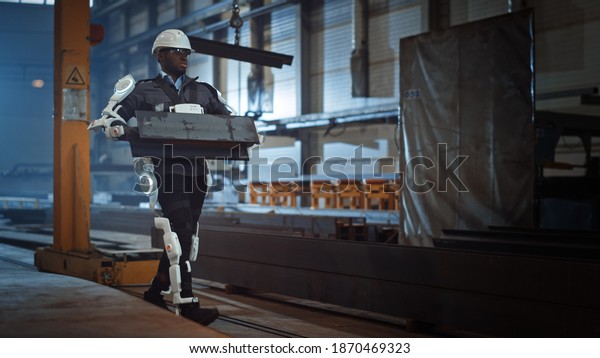 Black African American Engineer is Testing a\
Futuristic Bionic Exoskeleton and Proudly Wearing it in a Heavy\
Steel Industry Factory. Powered Mobile Machine Shell made for\
Helping Workers.