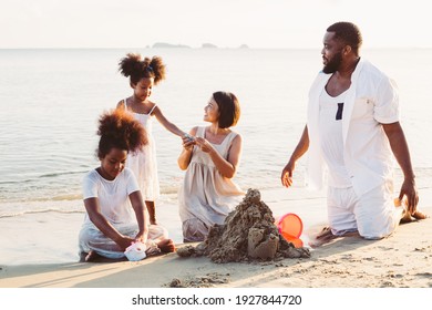 Black African American Family Playing And Building Sand Castle At Tropical Beach In Summer. Little Girl Talking With Asian Mother. Travel Vacation On Holiday Concept