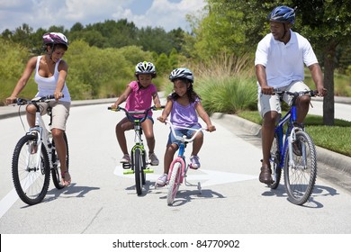 A Black African American Family Of Two Parents And Two Children, Two Girls, Cycling Together.