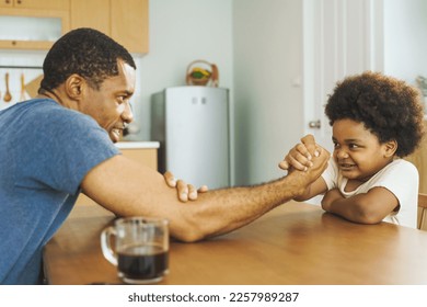 Black African American father competing in arm wrestling with his little boy in kitchen at home - Powered by Shutterstock