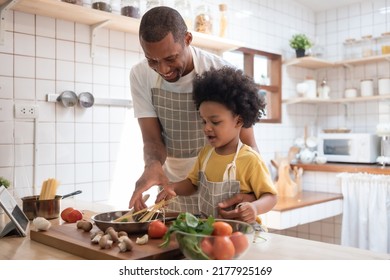Black African American Father teaching his Afro son cooking in kitchen at home. BeH3althy