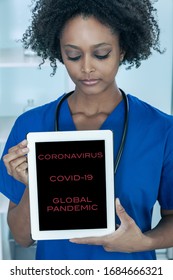 Black African American Female Medical Doctor In A Hospital Holding A Tablet Computer With Coronavirus COVID-19 Pandemic Text