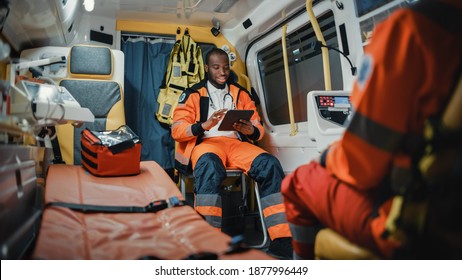 Black African American Paramedic Using Tablet Computer while Riding in an Ambulance Vehicle for an Emergency. Emergency Medical Technicians are on Their Way to a Call Outside the Healthcare Hospital. - Powered by Shutterstock