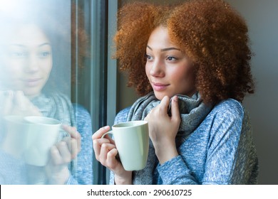 Black African American teenage girl drinking a hot beverage and looking through a window