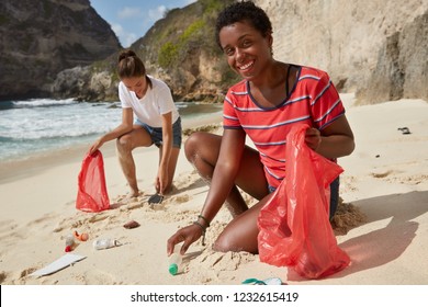 Black African American woman and her companion pick up recyclable plastic bottles and other rubbish, involved in volunteer work, pose at beach, being environmentally friendly. Cleaning concept - Powered by Shutterstock