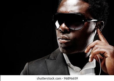 Black African Bodyguard Or Secret Agent On A Dark Background With Dramatic Lighting Gesture Towards Camera Wearing A Suit