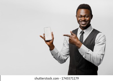 Black African Business Man Points To His Phone. Electronic Store Worker. Successful People Lifestyle Advert. You Can Win A Prize In Online Bet. Man Separete White Background