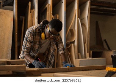 Black African Carpenter professional craftsmen wear safety gear. He was measuring the size and making wooden plank symbols on the table for the craft. in Carpenter and wood craftsmanship concept