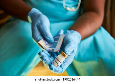 A Black African Doctor Sitting Wearing Blue Surgical Gloves And Scrubs Selling The Covid 19 Vaccine For Cash