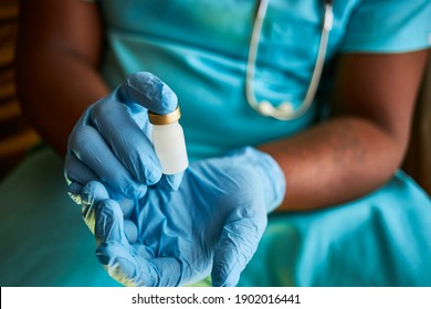 A Black African Doctor Wearing Surgical Scrubs And Gloves Presenting A Vial Of Covid 19 Vaccine In His Hands