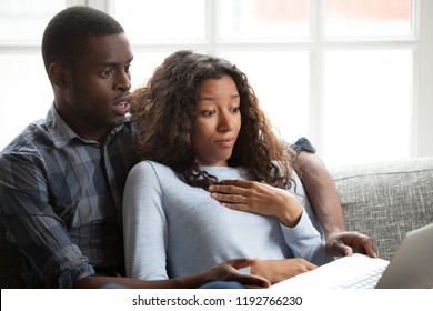 Black african emotional surprised frightened millennial married couple in love wife husband spend free time together sitting on couch at home. People watching online internet tv thriller scary movie
