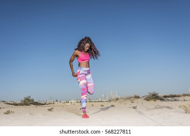 Black African Female Athlete Stretching In The Hot Desert Wearing Bright Colored Workout Gear 