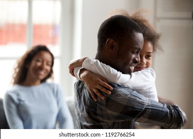 Black African happy family together at home. Close up loving American father strong embrace lovely sweet daughter smiling mother on background sitting on couch. Reunion happy wellbeing family concept