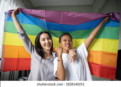 Black African LGBT Woman Holding LGBTQ Rainbow Flag With Asian LGBT Woman Upside Down, New Member Of Gay Pride Movement Concept