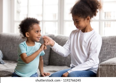 Black African little brother and sister sitting on couch at home. Small american children reconcile after fight or quarrelling making peace with hand gesture joining pinkies swear be friends forever