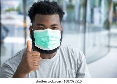 Black African man pointing thumb up to face mask usage, concept of taking precaution measure, social distancing, new normal lifestyle, wear mask while waiting for coronavirus COVID-19 vaccine