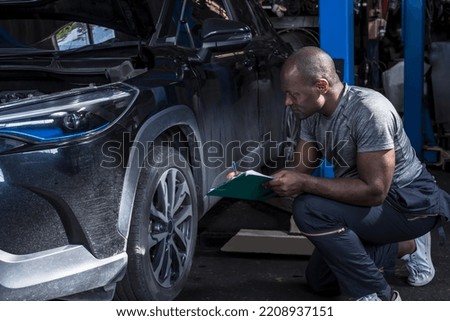 Black African mechanic holding clipboard checking car problem lists in auto repair shop, African American car technician working in garage, black mechanic man ,car repair and maintenance concept