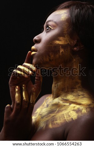 black african model covered painted with a glod paint posing for the bauty portrait, skin colored with paint