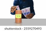 Black African person putting west African CFA franc note currency in brown wooden cylindrical savings container box and holding more cash in other hand. Businessman keeping money concept