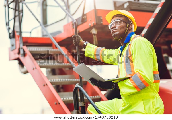 Black African Staff foreman intend to work\
loading worker using laptop computer to control cargo shipping in\
logistic warehouse.