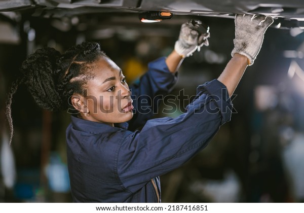 Black african woman mechanic staff worker work\
service under car in dirty\
garage