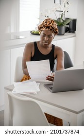 Black African Woman Working From Home, Going Through Paperwork. Laptop And Smartphone On Home Office Table