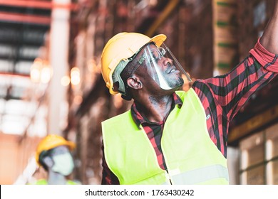 Black African worker wear protective face shield and helmet check stock in warehouse. Concept of new normal work in industry, factory after Covid 19 pandemic