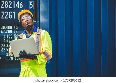 Black African worker working in logistic shipping using laptop to control loading containers at port cargo for import export goods foreman looking high for future