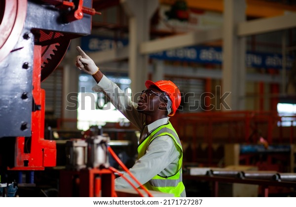A black African-American male engineer in a hard hat\
inspects the quality of industrial machines at a steel mill. The\
concept of dividing production in heavy industrial plants.\
Engineer. Worker. 