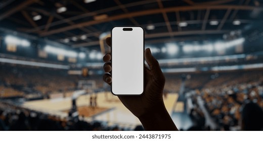 Black African-American man using smartphone with a blank screen during a game on basketball arena, perfect for showcasing apps or designs with a backdrop of live sports and enthusiastic fans - Powered by Shutterstock