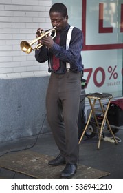 Black African-american Trumpet Player Wearing A Blue Shirt And Red Tie With White Suspenders Playing Jazz Music Outside As A Busker