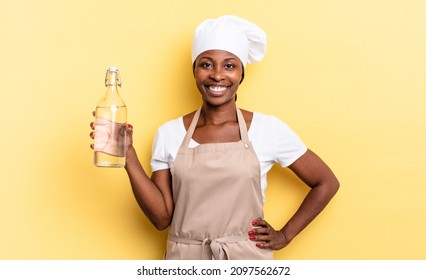 Black Afro Chef Woman Smiling Happily With A Hand On Hip And Confident, Positive, Proud And Friendly Attitude Holding A Water Bottle