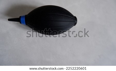 A black air blower blows dust on a lens with a dusty-white floor as a background, placed near the window resulting in a shadow
