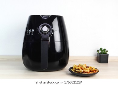 a black air fryer or oil free fryer appliance is on the wooden table in the kitchen with deep fried banana chips and small plant in the pot ( air fryer ) during dinner with happy family member in home - Shutterstock ID 1768821224