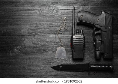 Black Airsoft Gun, Walkie Talkie Radio Station And Knife And Soldier Badge On The Black Flat Lay Background With Copy Space.