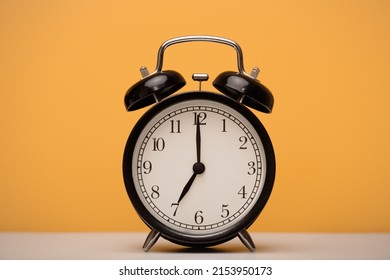 Black alarm clock close-up on a yellow background. The time is seven o'clock in the morning.