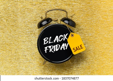 Black alarm clock with Black Friday written on it. Black friday sale concept. Alarm clock with price tag on golden glitter background