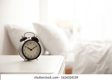 Black alarm clock on nightstand in morning. Space for text