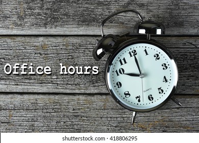 Black Alarm Clock On The Rusty Wooden Table With Word Office Hours