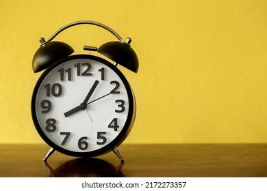 Black Alarm Clock On Wooden Board Over Yellow Background, 8 O'clock 5 Minutes