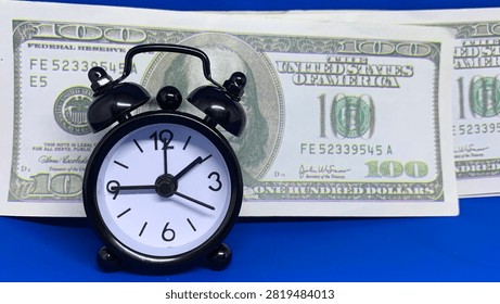 Black alarm clock positioned before a one-hundred-dollar bill, symbolizing the connection between time and money
