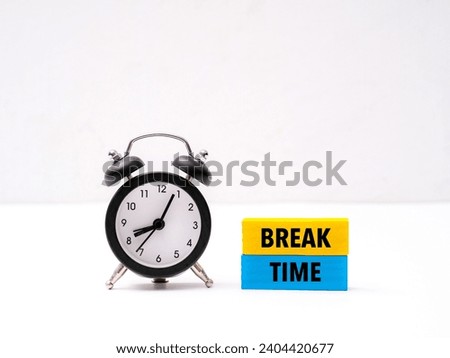 A black alarm clock sitting next to coloured wooden block with word “BREAK TIME” on it
