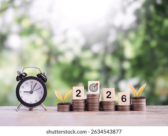 Black alarm clock, Wooden blocks with the number 2026 and plants growing up on stack of coins. The concept of saving money for manage time to success business in year 2026