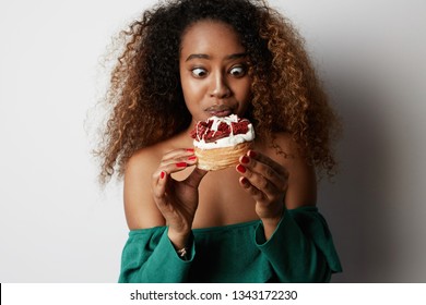 Black american african woman with Curly afro hair style making a mess eating a huge fancy dessert over white background.