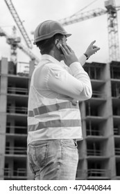 Black Anf White Rear View Portrait Of Construction Engineer Talking By Phone And Pointing At Building Site