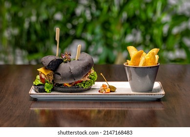 Black Angus Burger Cut In Half Served With Potatoes On A Wooden Table With Floral Backround.